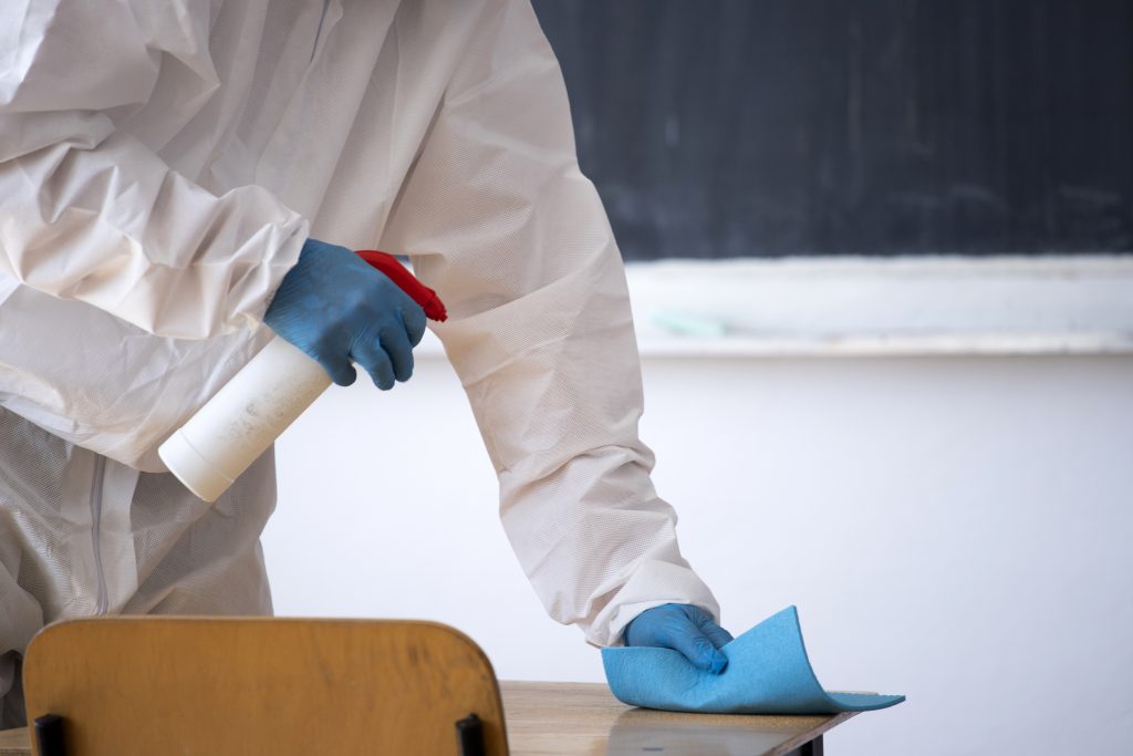 Man in a uniform performing a disinfection on a school table